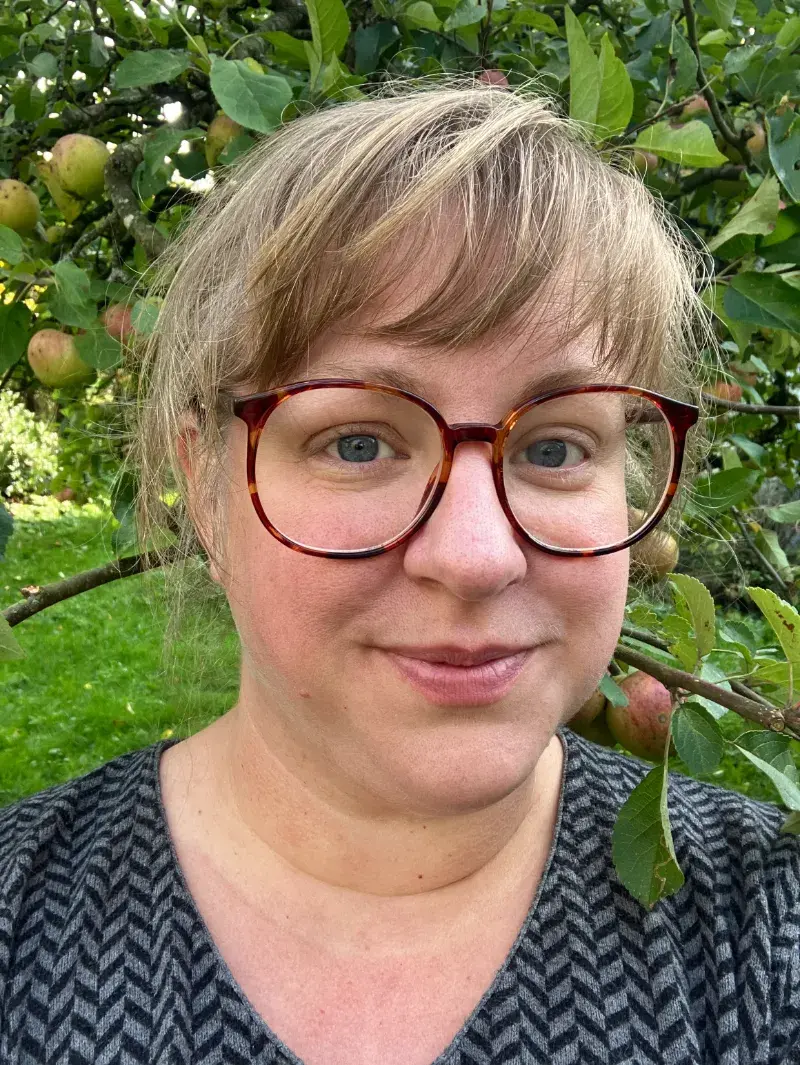 Li Bramstedt, ägare av Kvistar och rötter, framför ett äppelträd.
